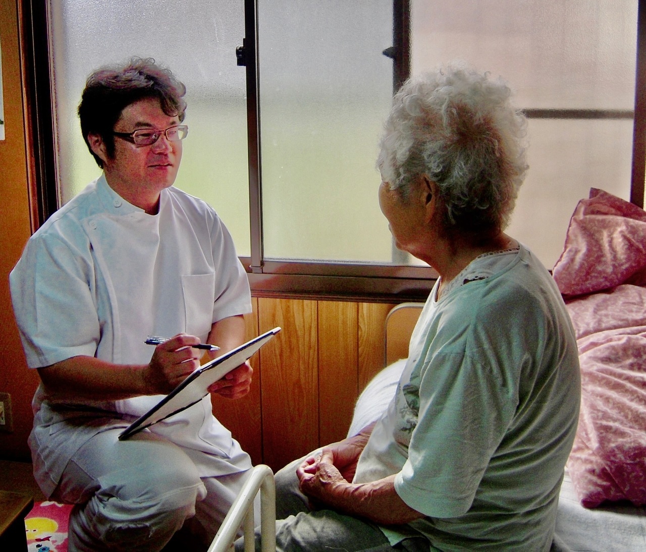 鍼灸施術前に高齢女性と話す白衣の男性鍼灸師
