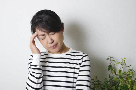 頭痛でこめかみに手を添える女性の写真